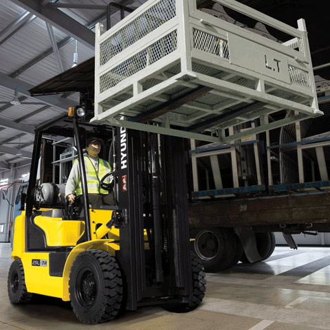 Carrello elevatore a forche gpl Hyundai 25l-7a con operatore impegnato nel sollevamento di un contenitore a gabbia